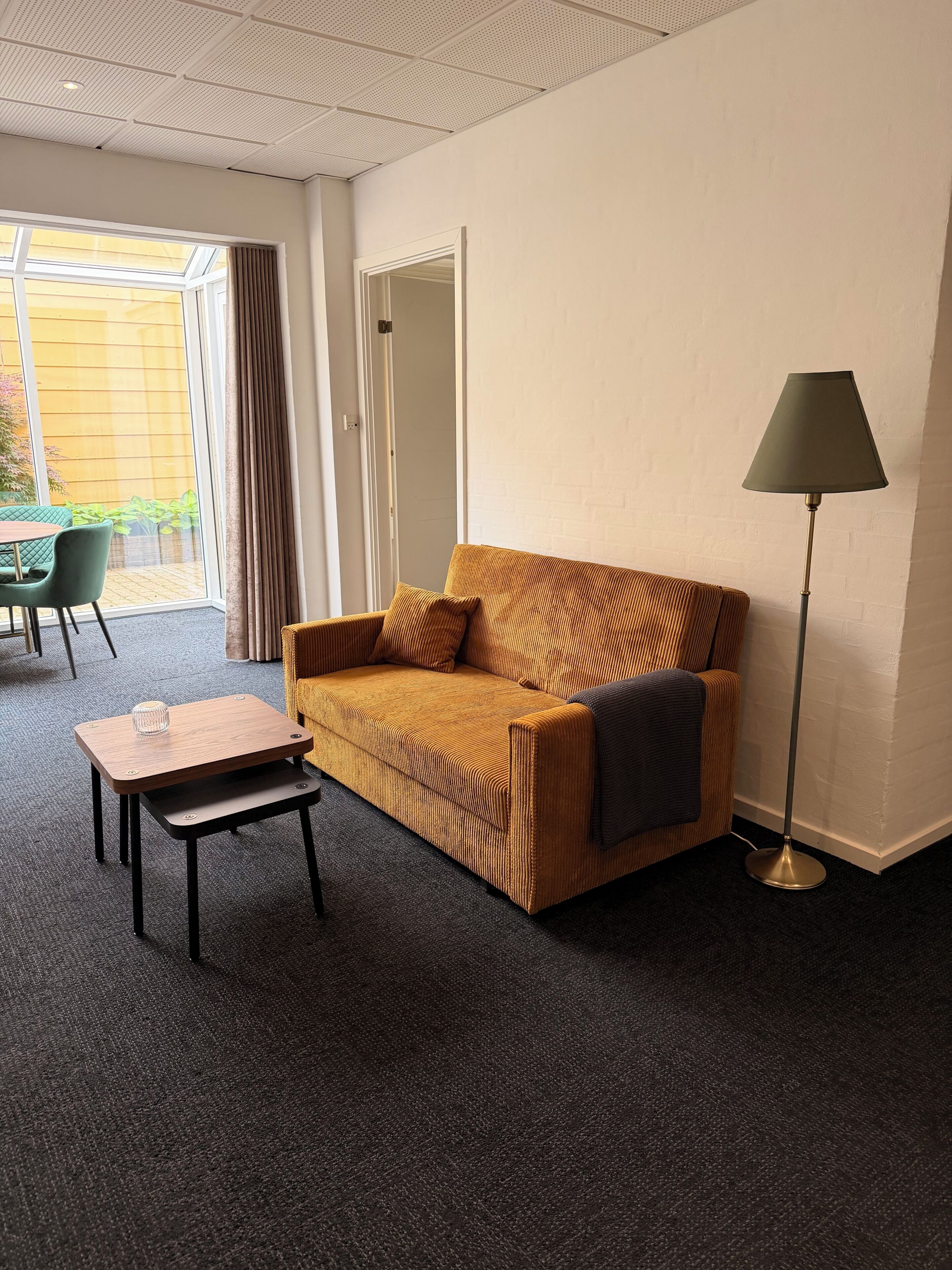 Una habitación con sofá, una mesita, una lámpara de pie y una puerta corrediza que da a un espacio al aire libre.