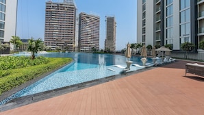 Un espace piscine doté d’une terrasse carrelée, de chaises longues et de parasols.