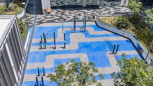 Un espace extérieur aménagé pour l’exercice physique, équipé d’appareils de musculation, doté d’un sol à motifs et entouré de verdure.