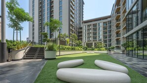 Un ensemble immobilier moderne comprenant plusieurs immeubles à étages, une cour intérieure avec une pelouse artificielle et un escalier menant aux étages supérieurs.