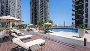 A rooftop pool area with sun loungers, umbrellas, and a view of the city skyline. - Free Housekeeping Visits During Your Stay - Stayshort - 1 Bedroom Escape in Dubai Creek Harbour That Sleeps 2 (Dubai)