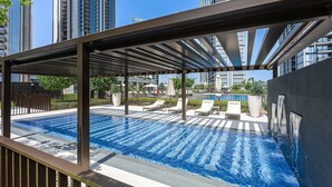 A rooftop pool with a view of high-rise buildings, lounge chairs, and a pergola structure. - Free Housekeeping Visits During Your Stay - Stayshort - 1 Bedroom Escape in Dubai Creek Harbour That Sleeps 2 (Dubai)