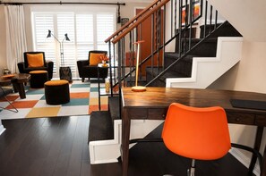 A modern living room with a staircase, a wooden desk, and orange chairs. - 2BR Condo | Pool & Hot Tub | Downtown Palm Springs | Mountain Views (Palm Springs)