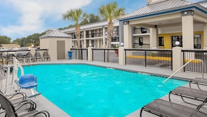 A swimming pool with lounge chairs, a building with a sign, and palm trees.