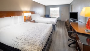 A hotel room with two beds, a desk, a TV, and a window.