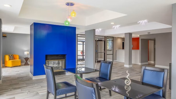 A modern dining area with a glass table and blue chairs, a fireplace, and a bright blue accent wall.
