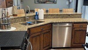 A modern kitchen with granite countertops, wooden cabinets, a stainless steel dishwasher, and a built-in oven.