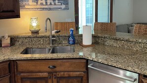 A kitchen with granite countertops, wooden cabinets, a stainless steel sink, a dish soap bottle, and a towel dispenser.
