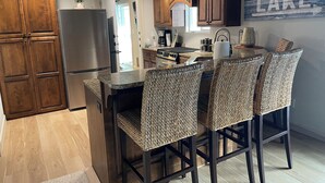 A kitchen with wooden cabinets, a stainless steel refrigerator, a granite countertop, and wicker bar stools.