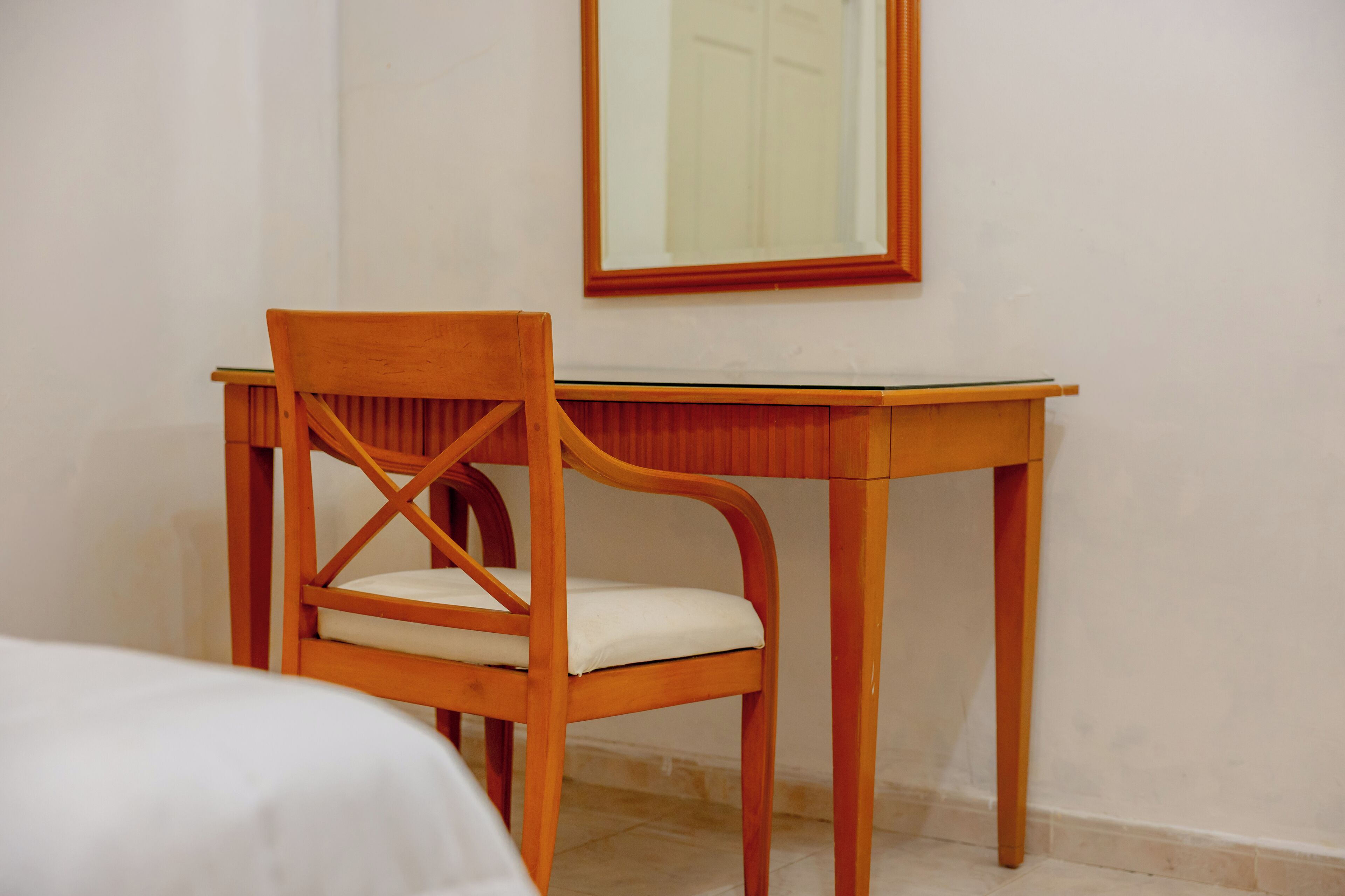Una silla de madera con asiento y respaldo acolchados, ubicada frente a un escritorio de madera con un espejo encima.