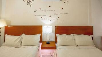 Una habitació d'hotel amb dos llits, una tauleta de nit amb una làmpada i una decoració mural amb text i papallones.