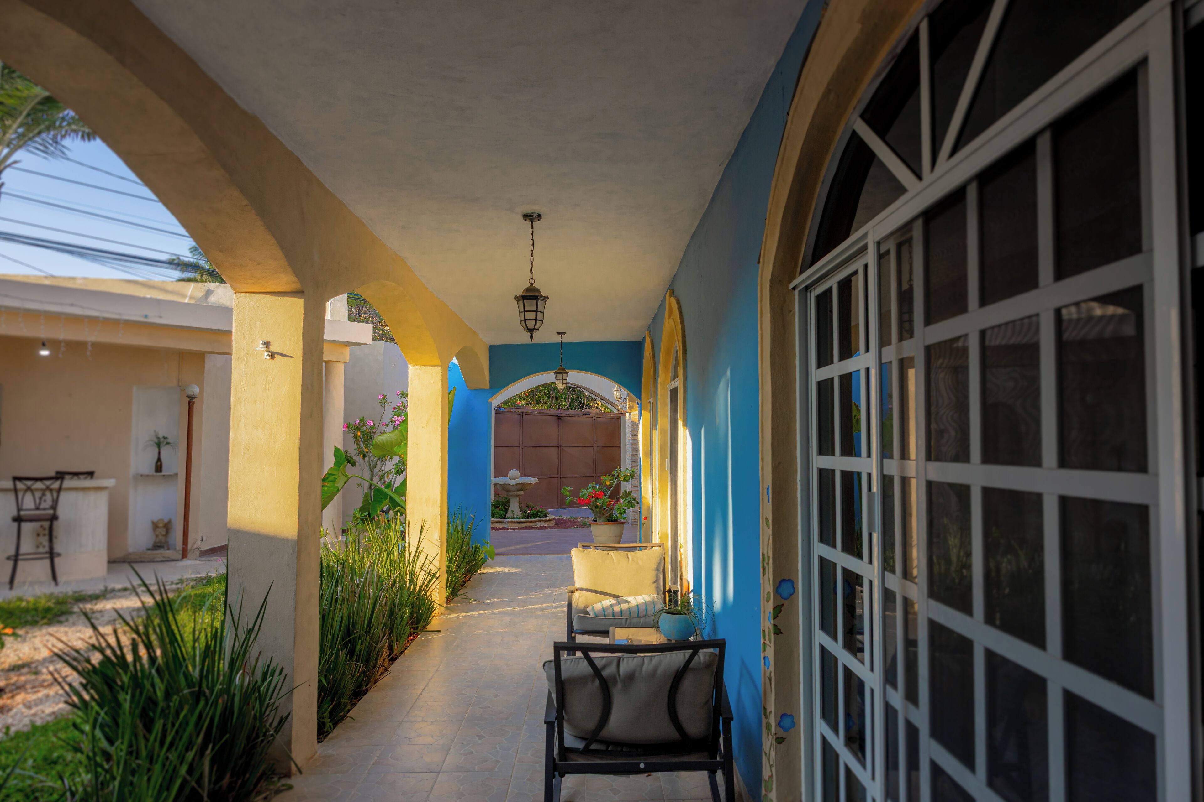 A covered outdoor corridor with a chair, potted plants, and a window.