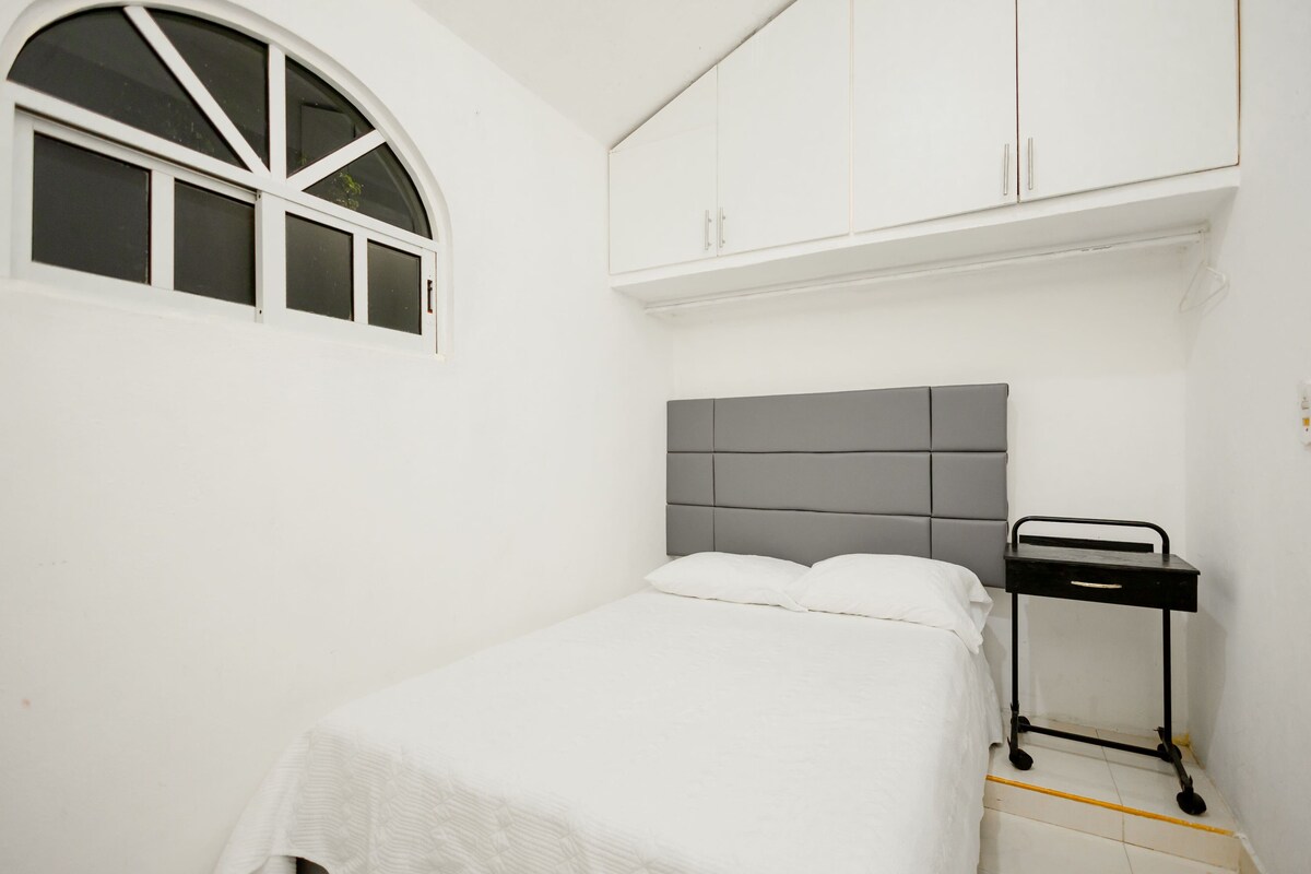 Un dormitorio con cama, ventana, armario y una mesita.