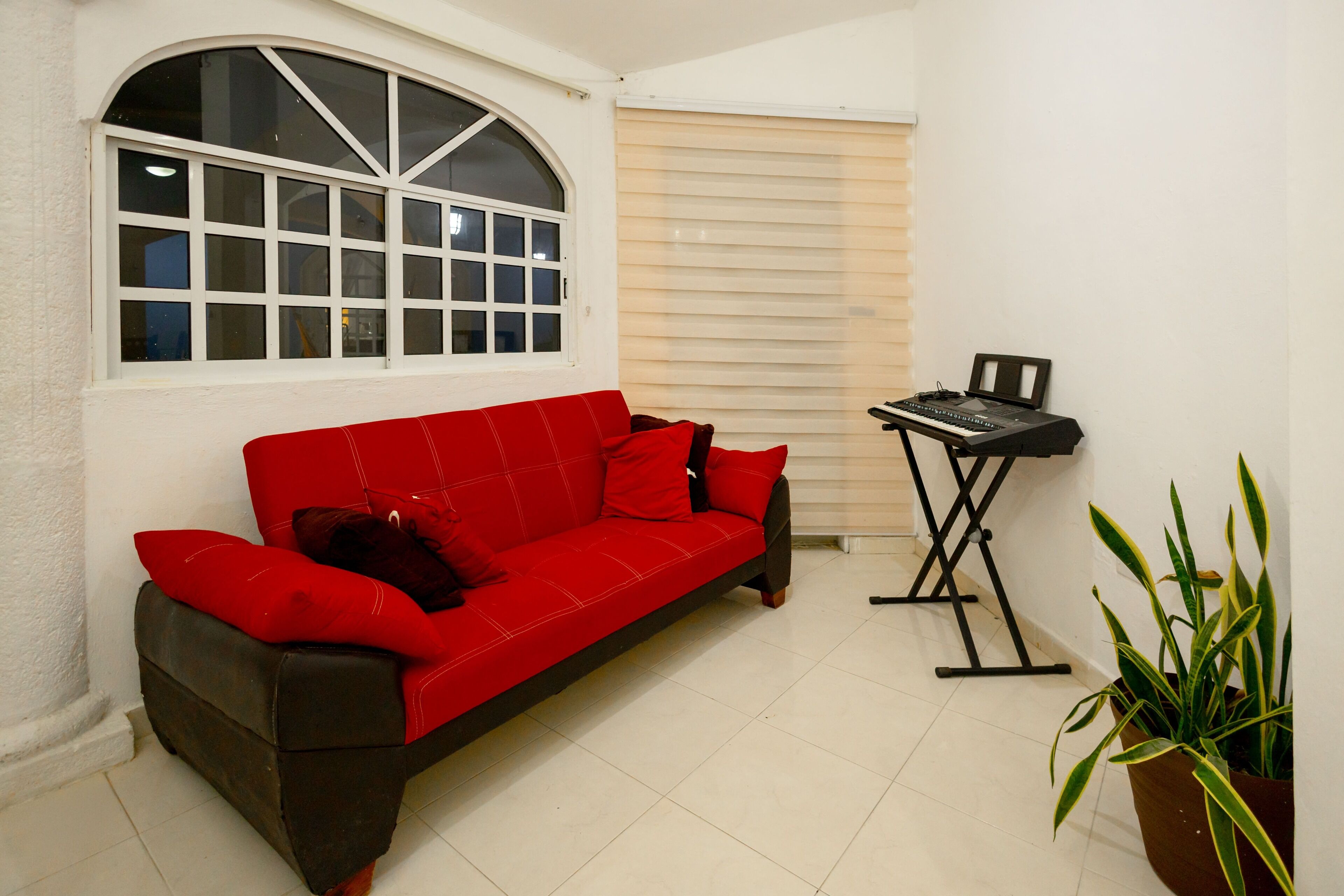 A red sofa with cushions, a small table with a keyboard, and a potted plant in a corner.