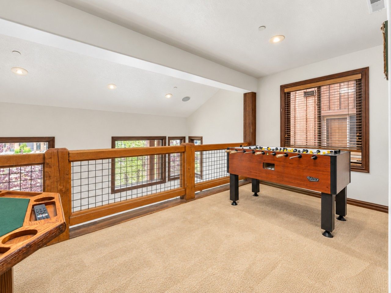 A room with a foosball table, a pool table, and a view through a window with blinds.