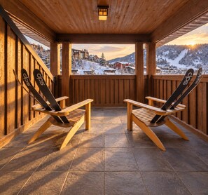 A wooden deck with two Adirondack chairs facing a snowy mountain view.