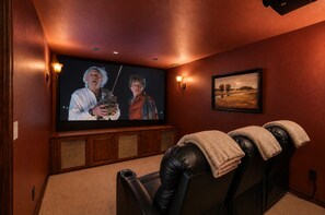 Un cine en casa con una pantalla grande, sillones reclinables de cuero y altavoces empotrados.