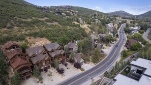 Zona residencial con una calle principal, casas de diversos estilos arquitectónicos y un paisaje montañoso al fondo.