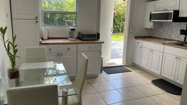 A modern kitchen with white cabinets, a glass dining table, and a view of greenery outside.