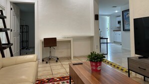 A modern living room with a sofa, a desk, a TV, and a potted plant.