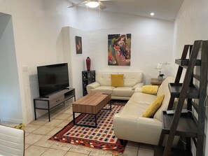 A living room with a TV, sofa, coffee table, patterned rug, and artwork on the wall.