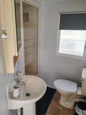 A bathroom with a sink, toilet, and a window with a blind. - Sunnyside41, Caravan - 8 Sleeps (Skegness)