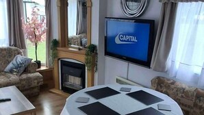 Olohuone, jossa on pyöreä pöytä, sohvia, takka, televisio ja näkymä ulos.