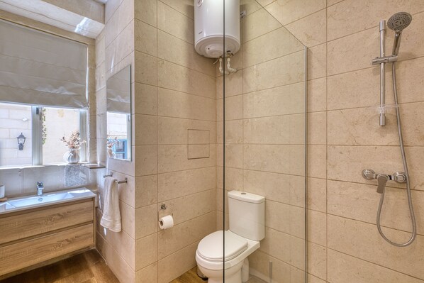 A bathroom with a toilet, a shower, a sink, and a mirror.