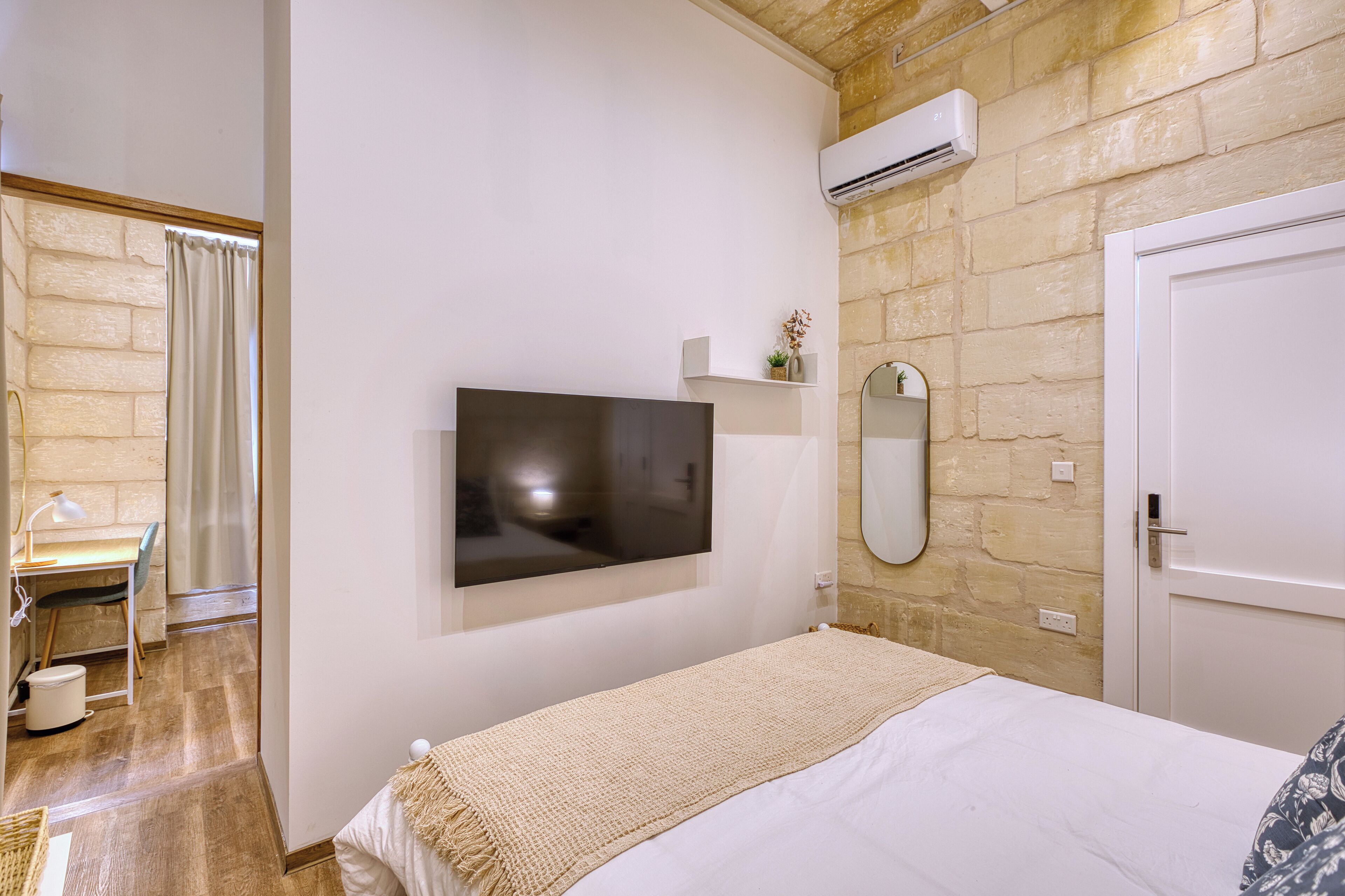 A bedroom with a bed, a TV mounted on the wall, a mirror, and a door.