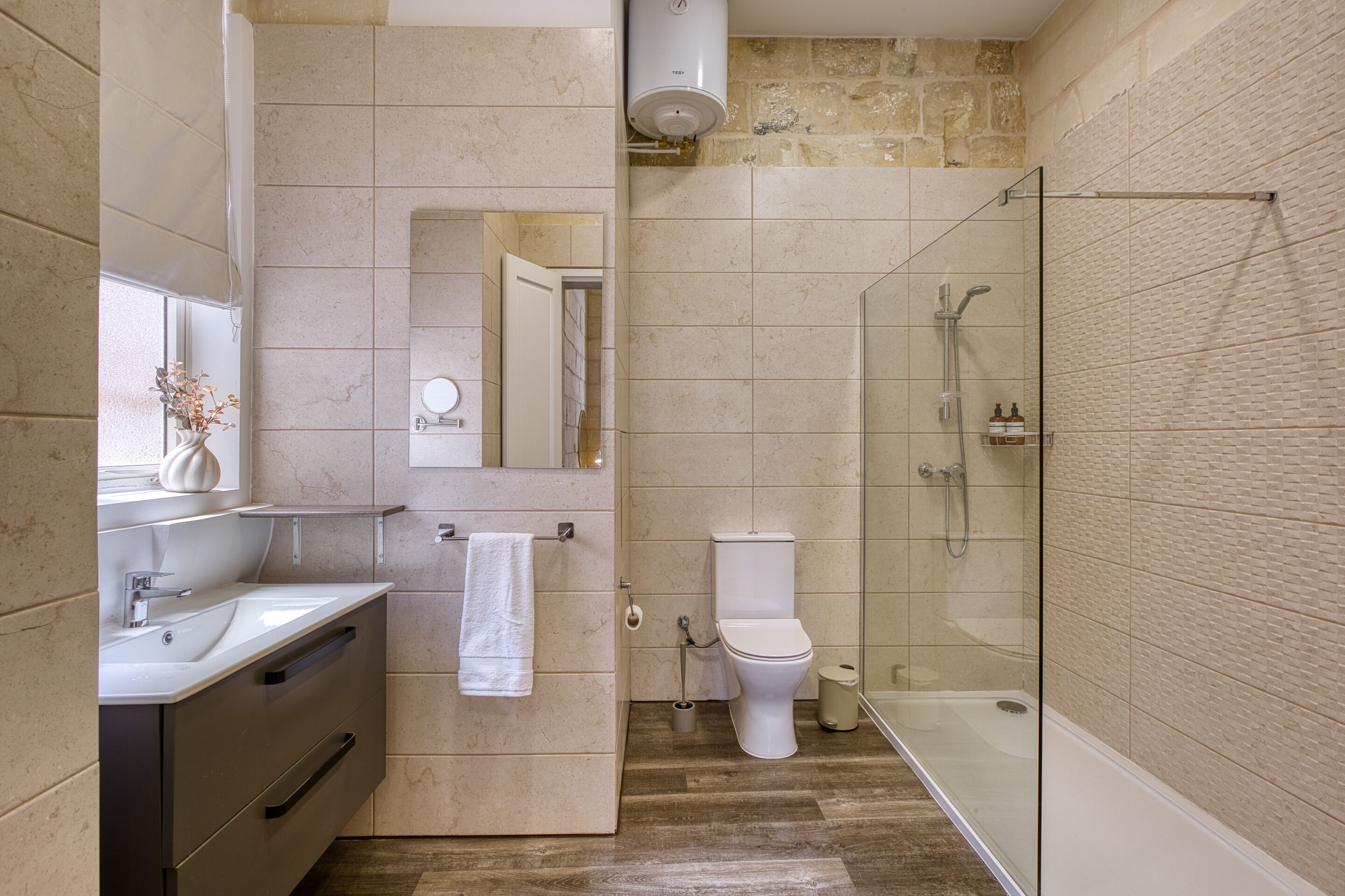 Un baño moderno con cabina de ducha de vidrio, inodoro y lavamanos con espejo.
