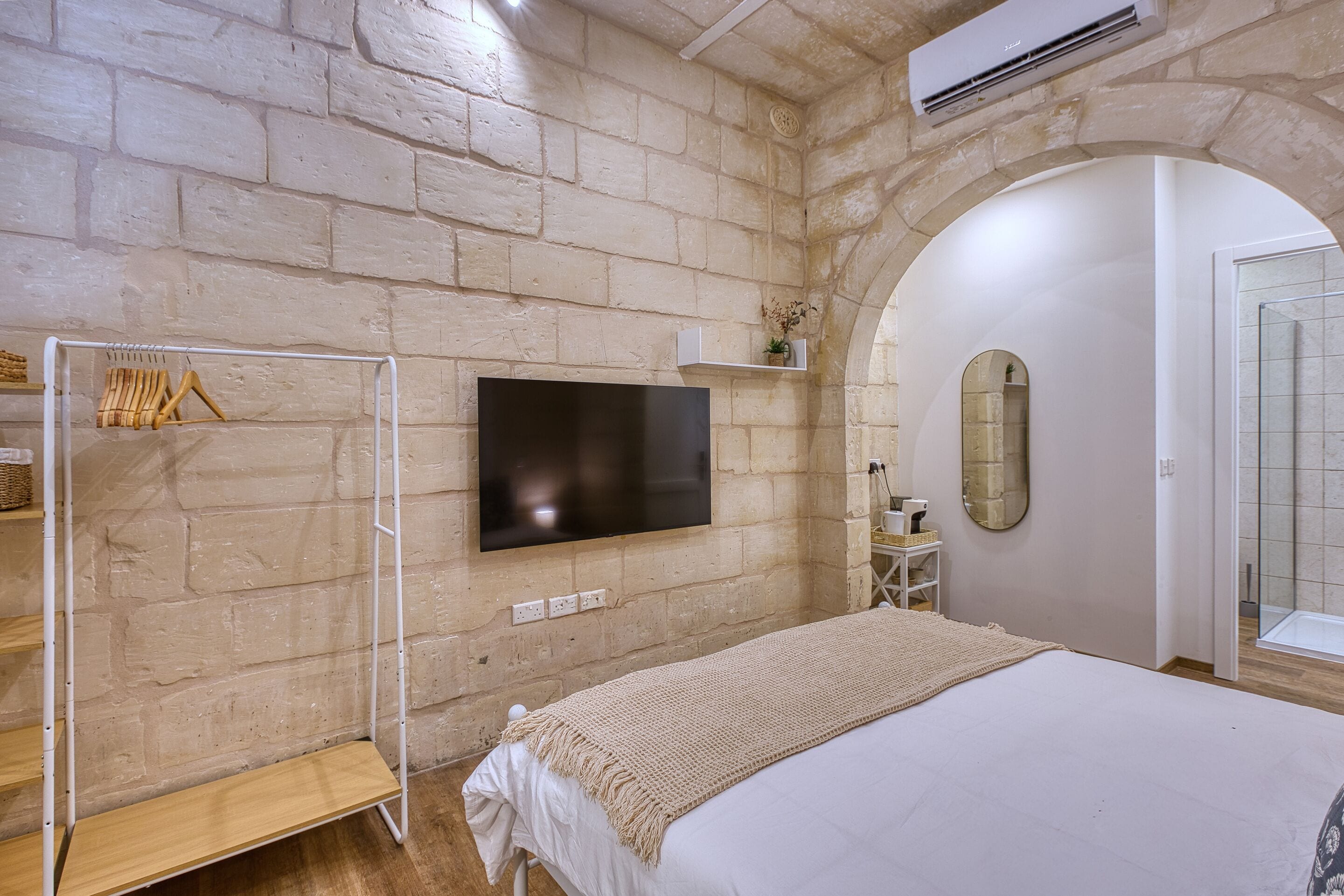 A bedroom with a large bed, a TV mounted on the wall, a wardrobe, and an arched doorway.