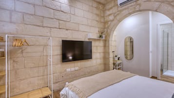 A bedroom with a large bed, a TV mounted on the wall, a wardrobe, and an arched doorway.