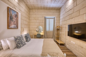 A bedroom with a bed, a desk, a mirror, a TV, and a window. - Dar Vitorja (Senglea)