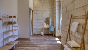 A room with a wooden floor, a desk with a chair, a mirror, a shelf with baskets, and a towel rack. - Dar Vitorja (Senglea)