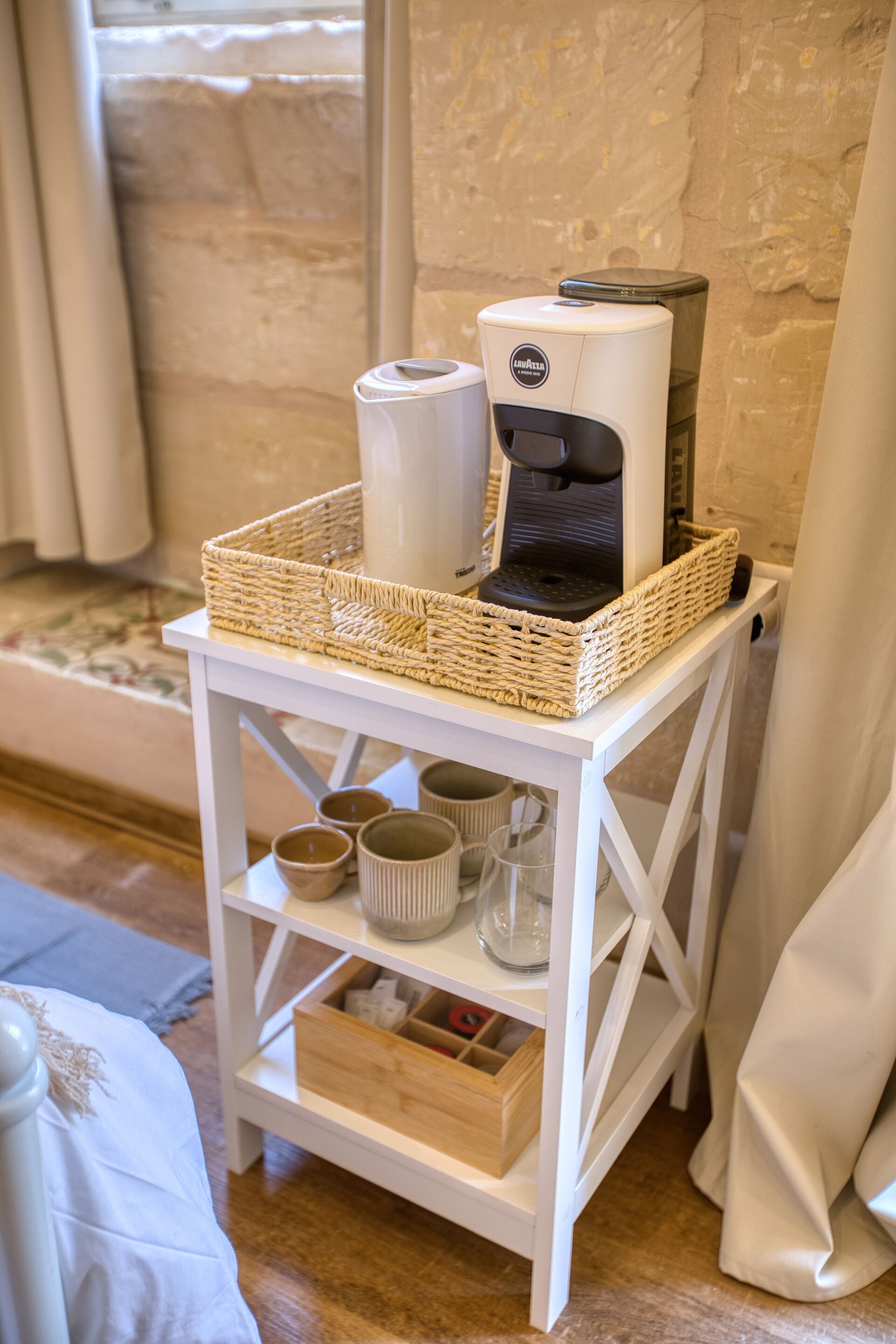 Eine weiße Kaffeemaschine auf einem weißen Regal, zusammen mit einem gewebten Korb, einer weißen Tasse und einem weißen Behälter.