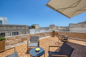 A rooftop terrace with outdoor seating, a table with a bowl, and a view of the cityscape. - Dar Vitorja (Senglea)