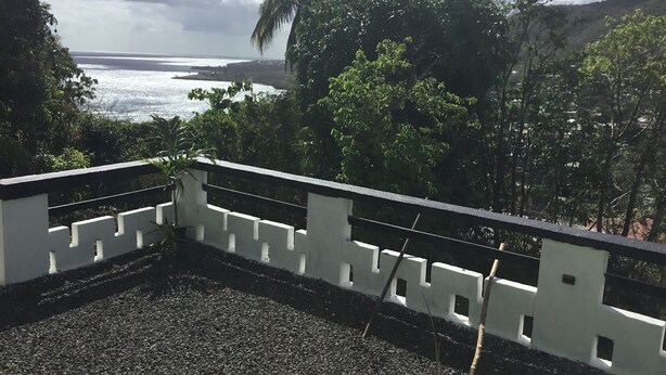 Een balkon met uitzicht op de oceaan en omliggend groen.