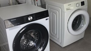 Twee voorladers, waarvan één met een digitaal display en de andere met een bedieningspaneel, in een wasserette met een wit aanrechtblad.
