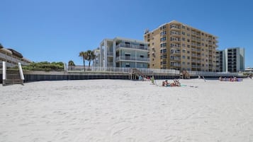 A beachfront hotel with multiple floors, a sandy beach in the foreground, and a clear blue sky.