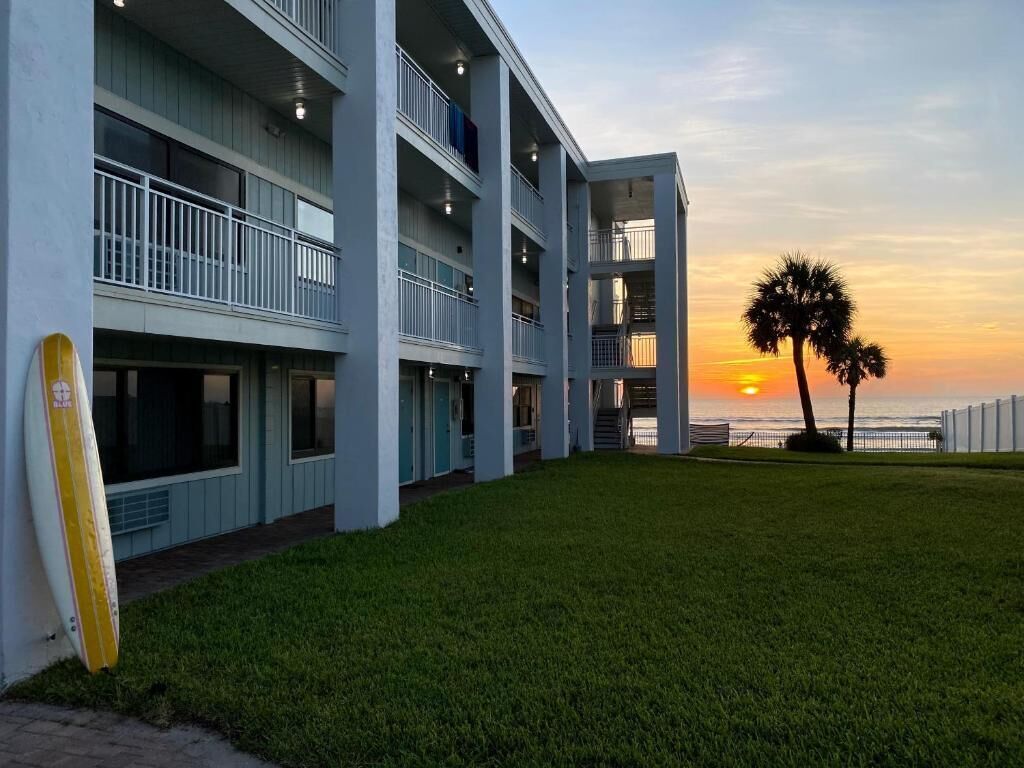 Un hôtel à plusieurs étages doté de balcons, d’une pelouse verdoyante et offrant une vue sur le coucher de soleil sur l’océan.