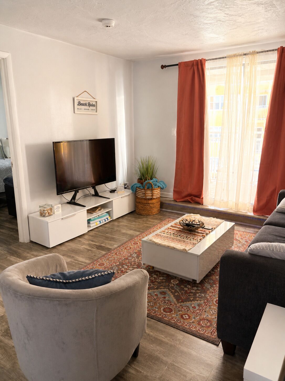 Una sala de estar con televisor de pantalla plana, un sofá, una mesa de centro y un ventanal con cortinas.