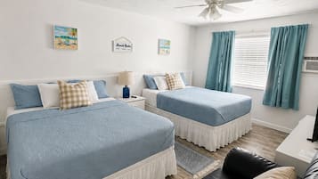 Une chambre avec deux lits, un ventilateur de plafond, un bureau et un canapé en cuir.