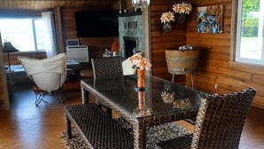 Un interior de madera con una mesa de comedor de cristal rodeada de sillas de mimbre, una chimenea y un televisor.