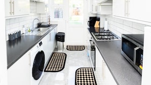 A modern kitchen with white cabinets, a stainless steel sink, a gas stove, and a microwave. - Joyden's Wood 2-bed Apt, Sleeps 5 With Parking (Dartford)