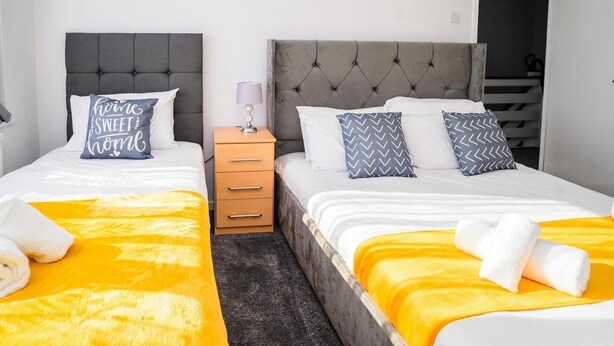 A hotel room with two beds, a wooden nightstand, and a lamp. - Joyden's Wood 2-bed Apt, Sleeps 5 With Parking (Dartford)