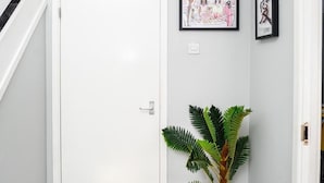 A hallway with a white door, a potted plant, and two framed pictures on the wall. - Joyden's Wood 2-bed Apt, Sleeps 5 With Parking (Dartford)