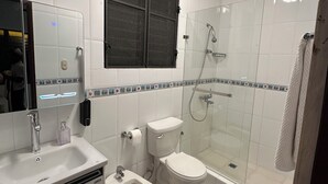 Une salle de bain comprenant des toilettes, un bidet, un lavabo, un miroir et une douche fermée par une paroi de verre.