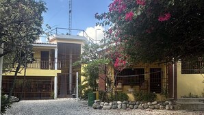 Un quartier résidentiel avec une allée en gravier, un bâtiment jaune doté d’une entrée fermée par un portail et un arbre aux fleurs roses.