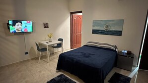 Une chambre à coucher comprenant un lit, un bureau, une chaise, une télévision, un ventilateur de plafond, un tableau et une table de chevet.