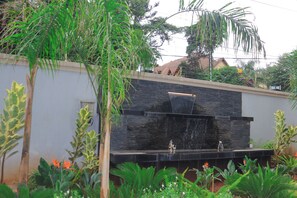 Una moderna fuente exterior con un muro de piedra, rodeada de exuberante vegetación y plantas tropicales.